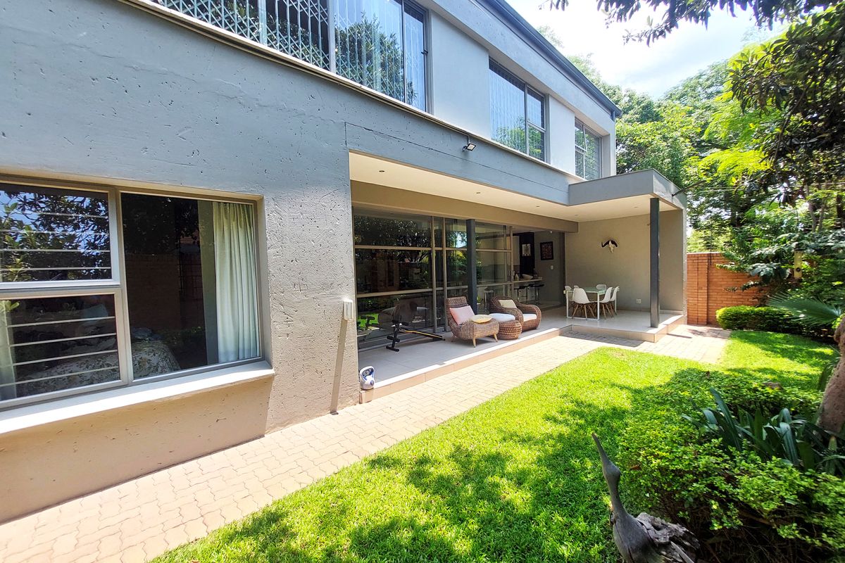 Rear view of the townhouse featuring a paved patio area, sliding glass doors, and a well-maintained garden with mature landscaping.