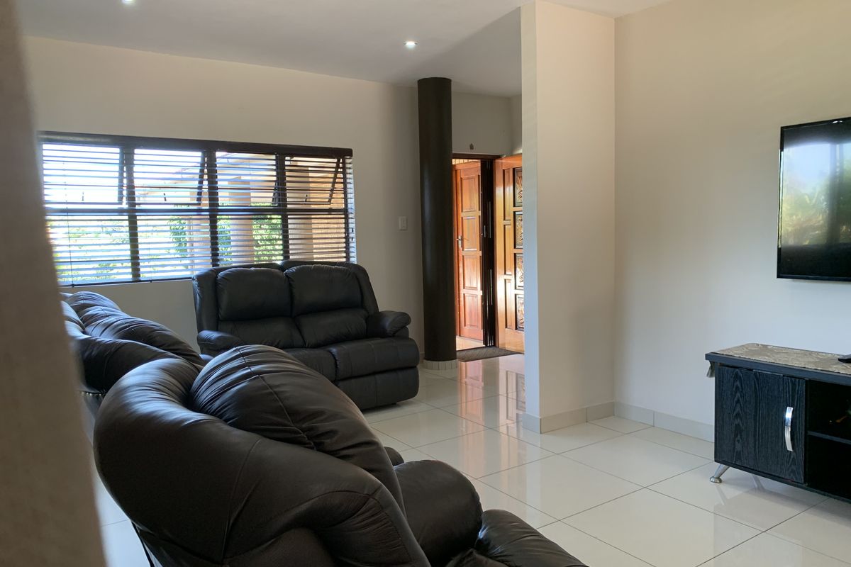 A spacious living room featuring polished floor tiles, recessed ceiling lighting, and a structural pillar, providing a clean and functional living space.