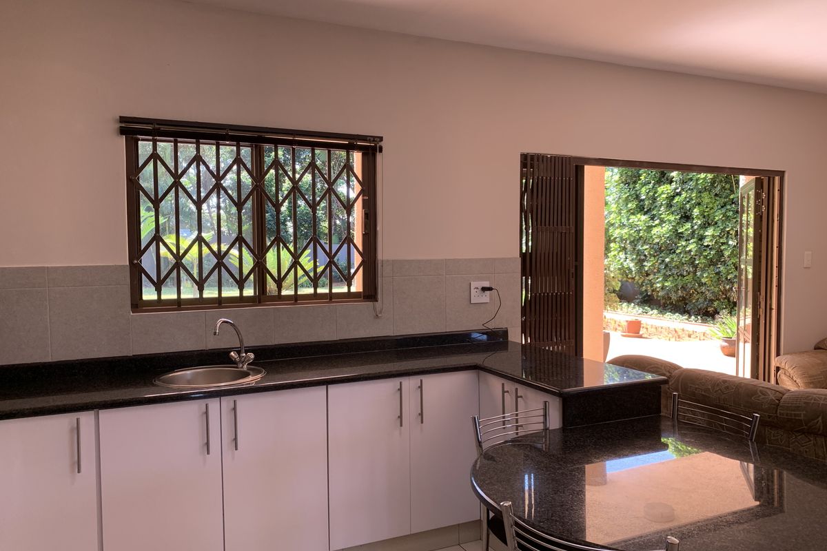 A functional kitchen area featuring granite countertops, white cabinetry, a stainless steel sink, and direct access to an outdoor patio space.