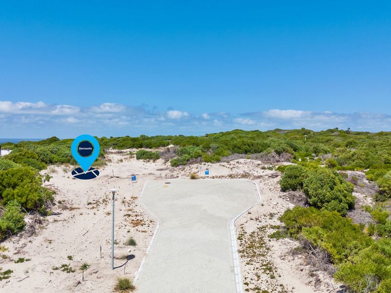 Aerial view of a vacant residential plot featuring a paved driveway entrance and surrounding coastal vegetation.