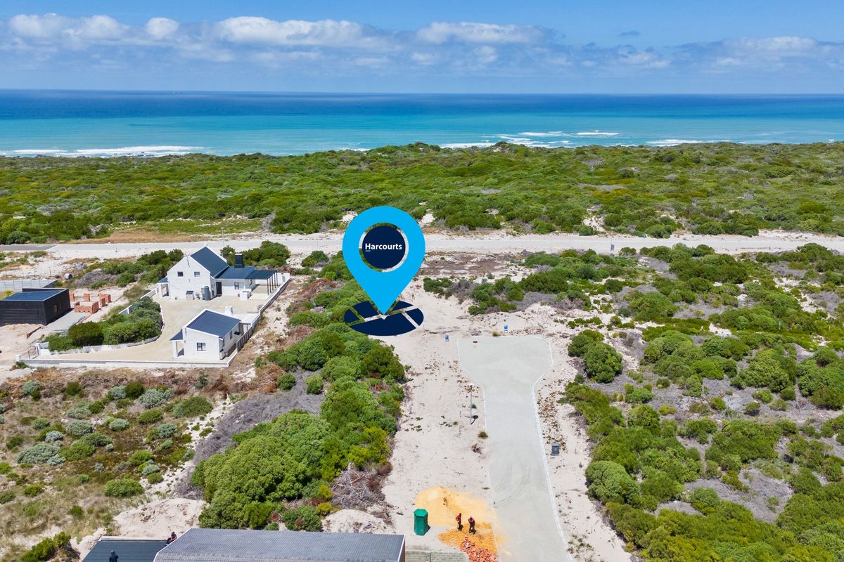 Aerial view of a vacant residential plot featuring a paved driveway, surrounded by coastal vegetation with ocean views in the background.