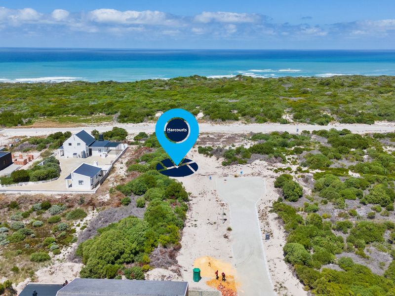 Aerial view of a vacant residential plot featuring a paved driveway, surrounded by coastal vegetation with ocean views in the background.