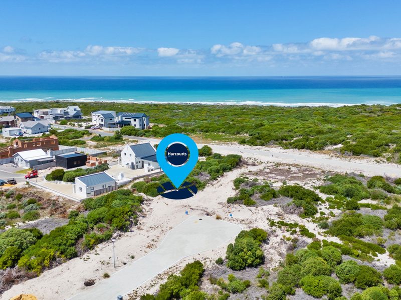 Aerial view of a vacant residential plot situated in a coastal development with paved road access and surrounding natural vegetation.