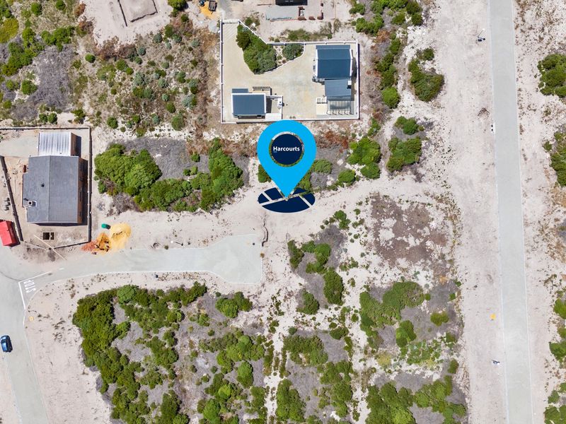 Aerial view of a vacant residential plot situated in a coastal development with established road access and surrounding natural vegetation.