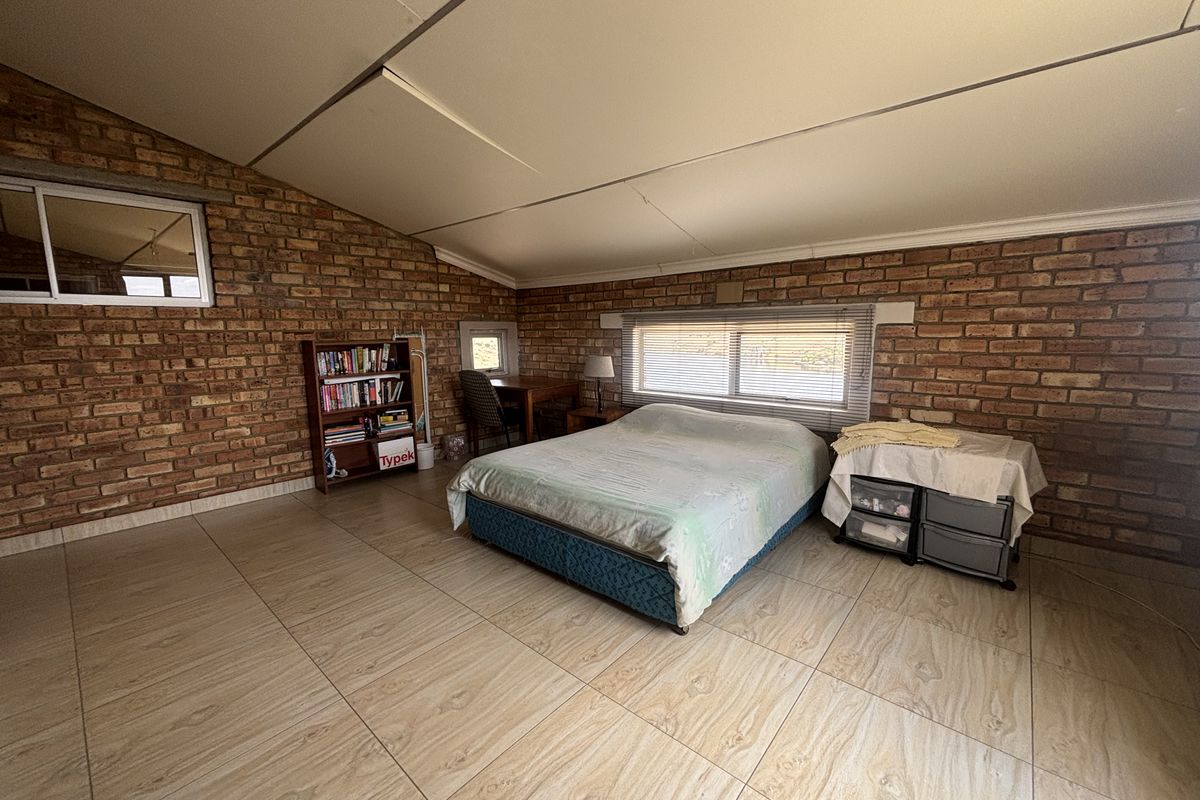 Spacious bedroom featuring exposed brick walls, large format floor tiles, and a sloped ceiling with integrated aluminium windows.