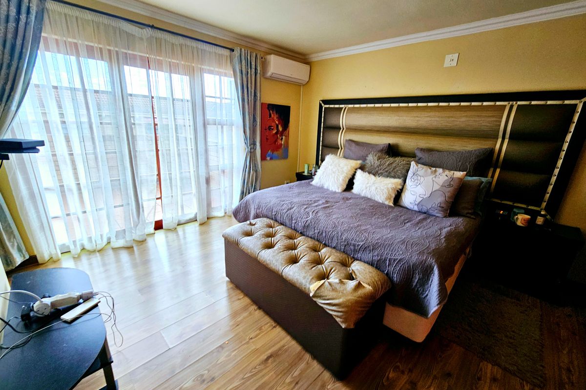 A spacious bedroom featuring laminate flooring, crown molding, a wall-mounted air conditioning unit, and large sliding glass doors providing access to the exterior.