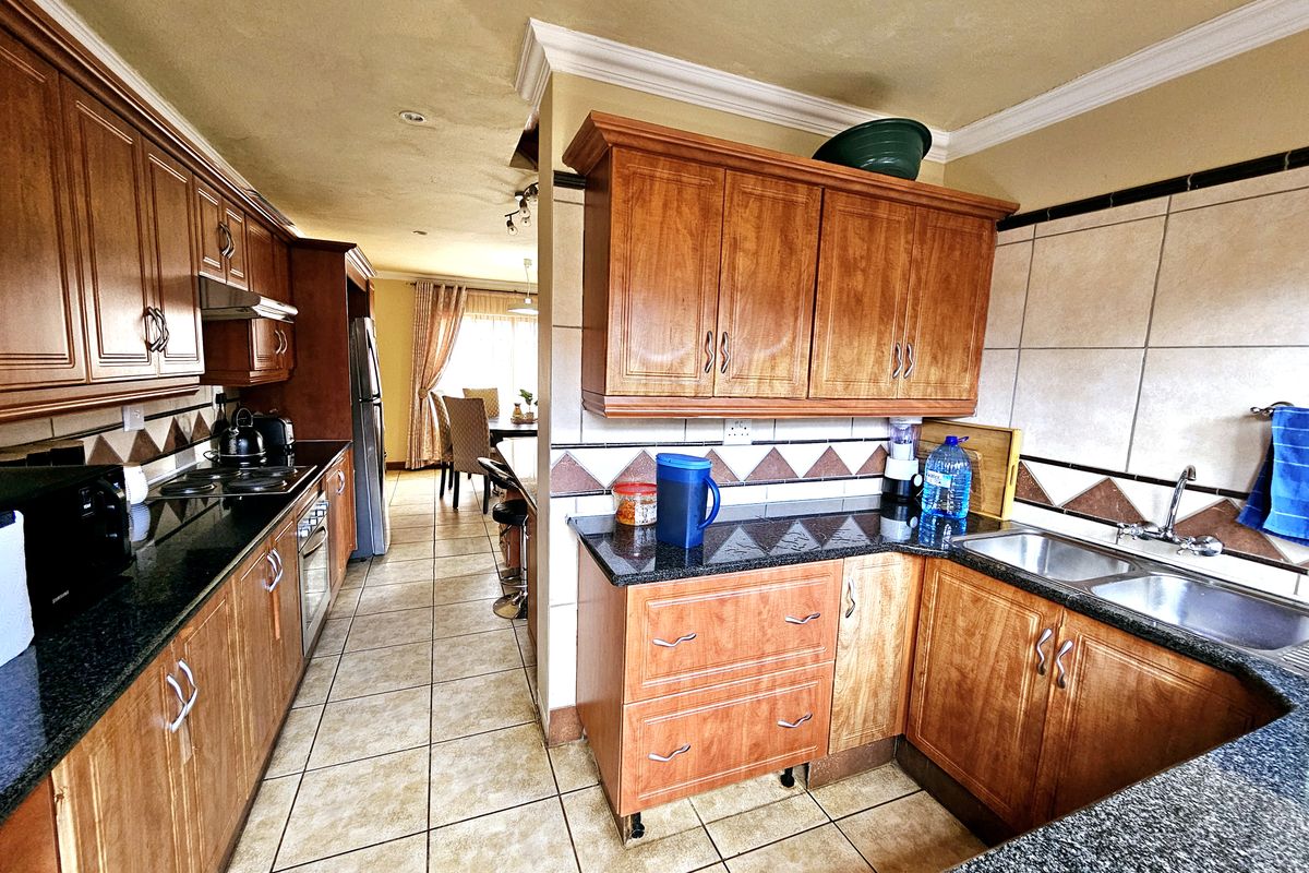 A functional kitchen featuring wooden cabinetry, granite countertops, and a double basin sink, with an open-plan layout leading to the dining area.