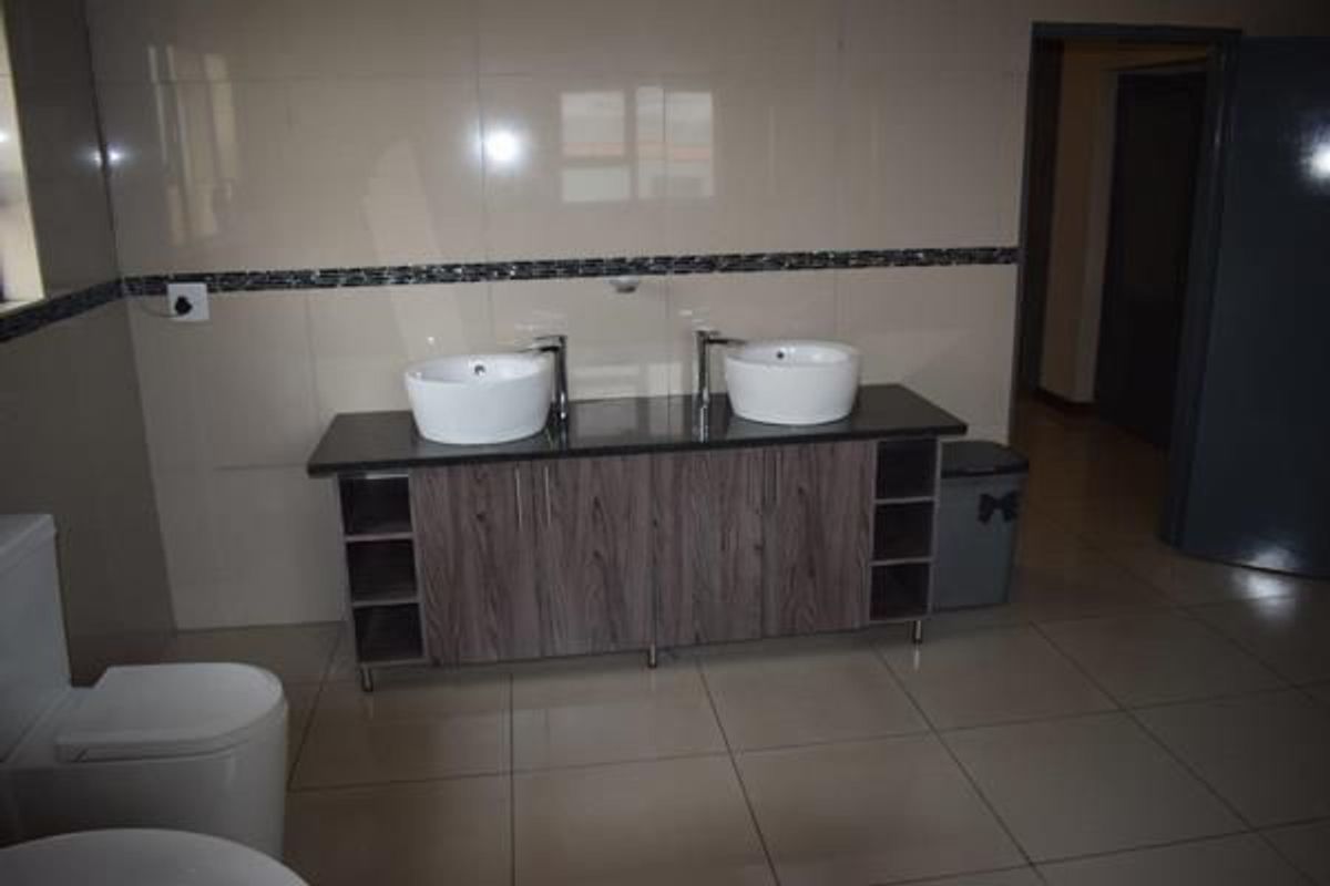 A modern bathroom featuring a double vanity with vessel sinks, dark stone countertop, wood-grain cabinetry, and tiled walls and flooring.