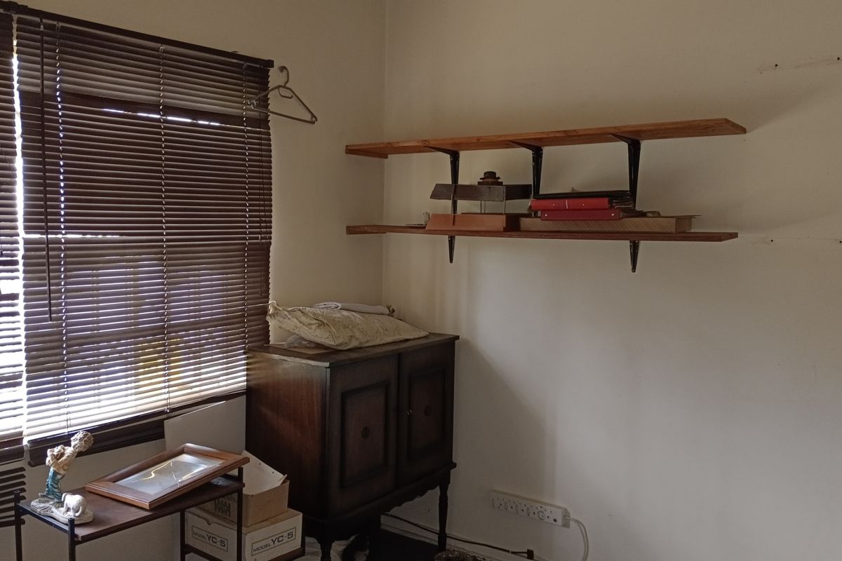 A bedroom corner featuring wall-mounted wooden shelving, venetian blinds, and an electrical power outlet.