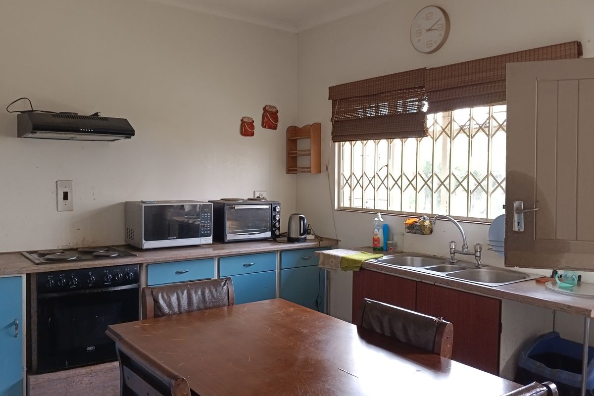A functional kitchen featuring built-in oven, electric hob, extractor fan, and double bowl sink with fitted cabinetry and security window bars.