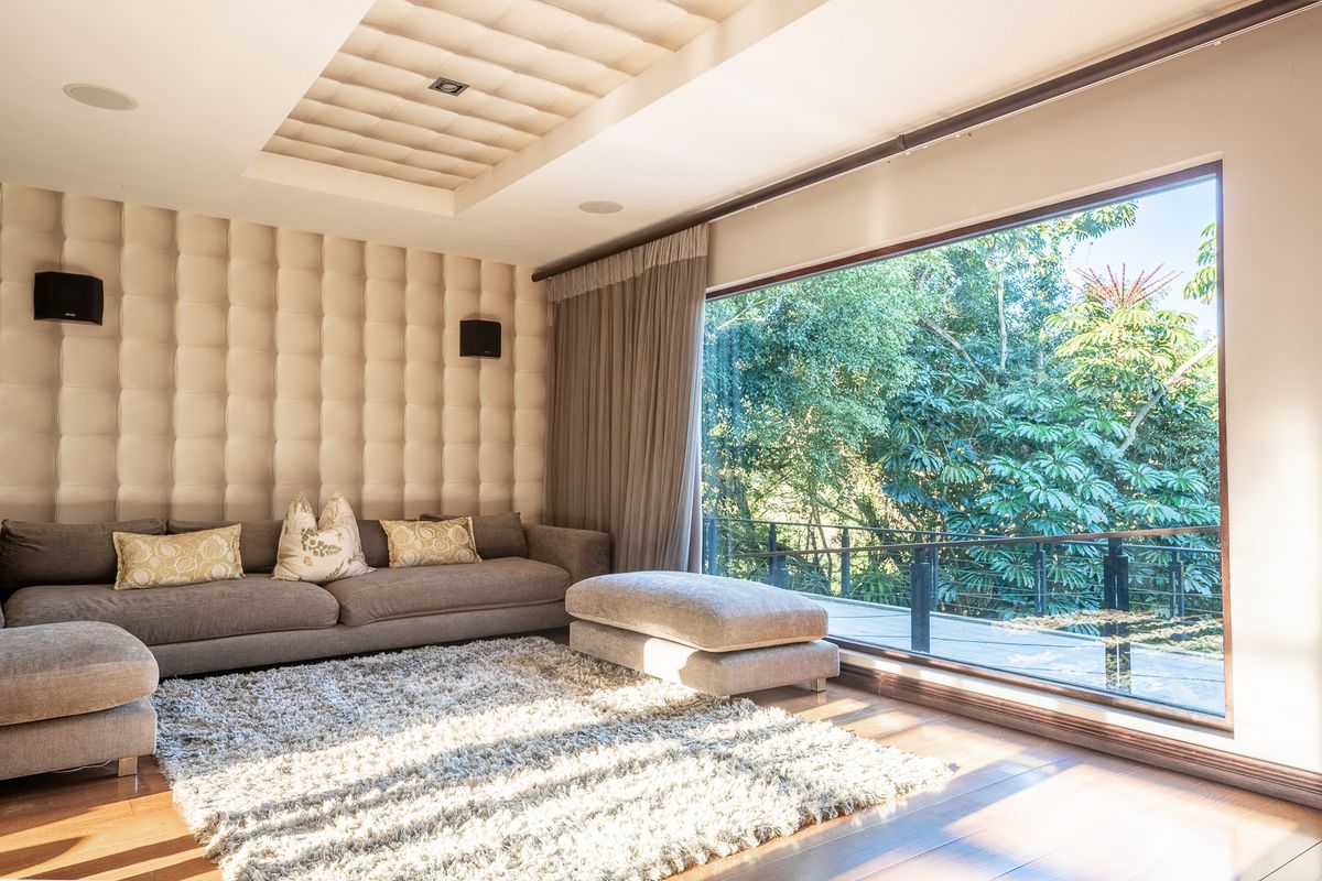 Sophisticated living room featuring custom upholstered wall paneling, recessed ceiling detail, and a large picture window offering serene views of the surrounding greenery.