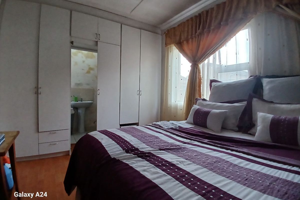 Bedroom featuring built-in cupboards and an adjoining ensuite bathroom with a pedestal basin, showing signs of wear and wall surface deterioration.