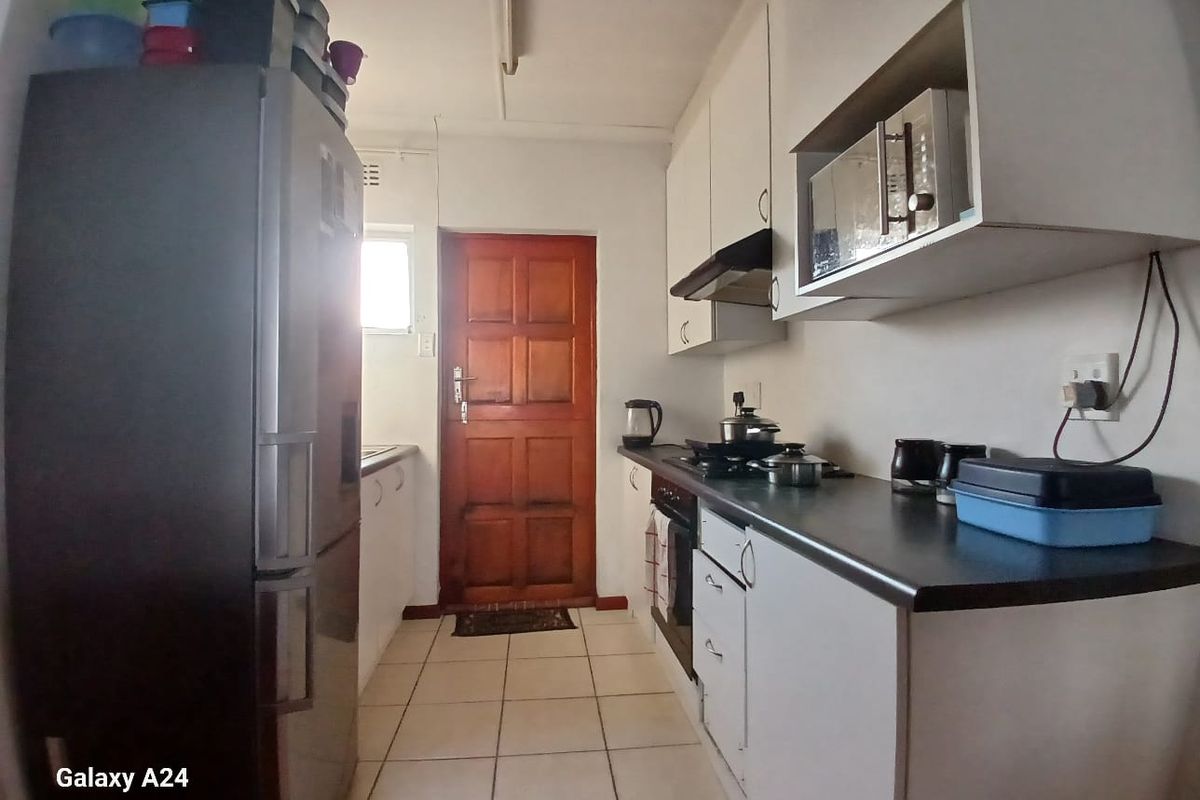 A functional galley-style kitchen featuring white cabinetry, dark laminate countertops, built-in oven, gas hob, and tiled flooring with direct access to an exterior door.