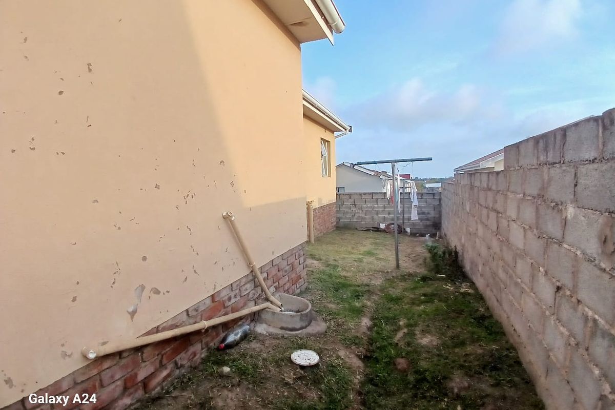 Rear exterior view of the property showing a side yard, boundary wall, and exterior wall finishes requiring maintenance.
