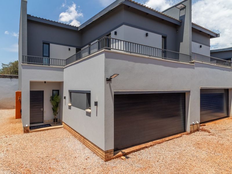 Modern townhouse exterior featuring a double garage, balcony with metal railing, and a gravel driveway area.
