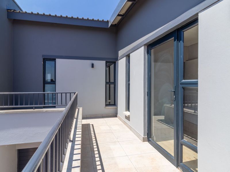 A modern, well-maintained balcony featuring tiled flooring, metal railings, and large glass sliding doors providing access to the interior.