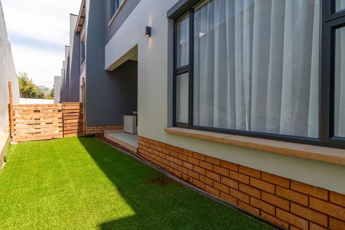A view of the rear exterior of the townhouse, featuring a small private garden with artificial turf and a paved patio area.
