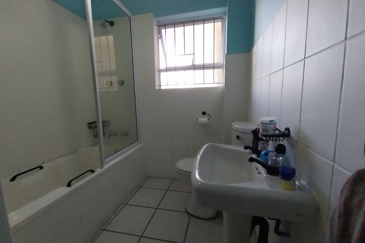 A functional bathroom featuring a pedestal sink, a bathtub with a glass shower screen, and a window with security bars.