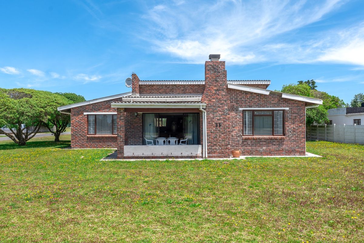 Rear view of a single-story brick house featuring a prominent chimney, a covered patio area, and a spacious surrounding garden.