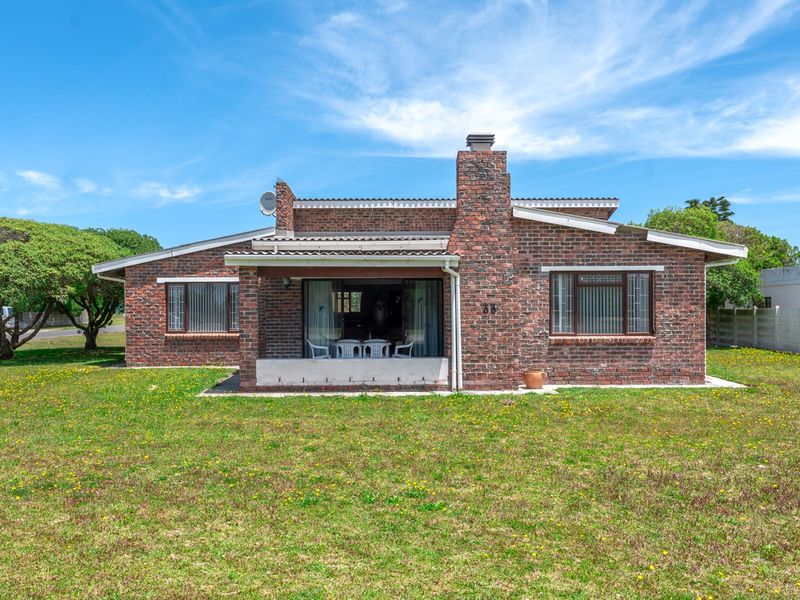 Rear view of a single-story brick house featuring a prominent chimney, a covered patio area, and a spacious surrounding garden.