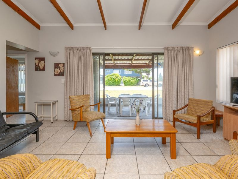 Spacious living room featuring exposed timber ceiling beams, ceramic floor tiles, and large sliding glass doors providing direct access to the outdoor patio area.