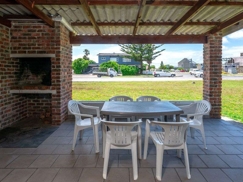 Covered outdoor patio featuring a built-in brick braai, tiled flooring, and exposed timber beams, overlooking a front garden and street view.
