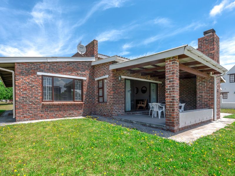 Rear view of a brick-clad house featuring a covered patio area, sliding glass doors, and a spacious garden setting.
