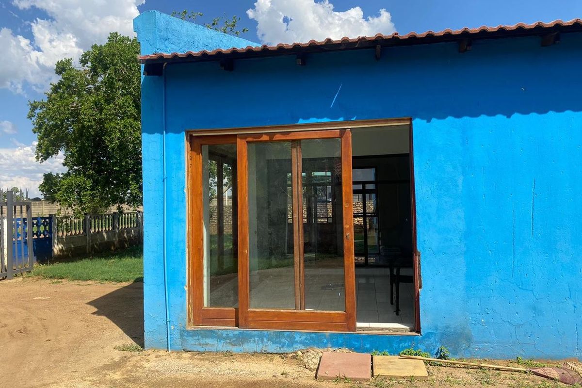 Rear exterior view of a blue painted house featuring a wooden sliding glass door and terracotta roof tiles.