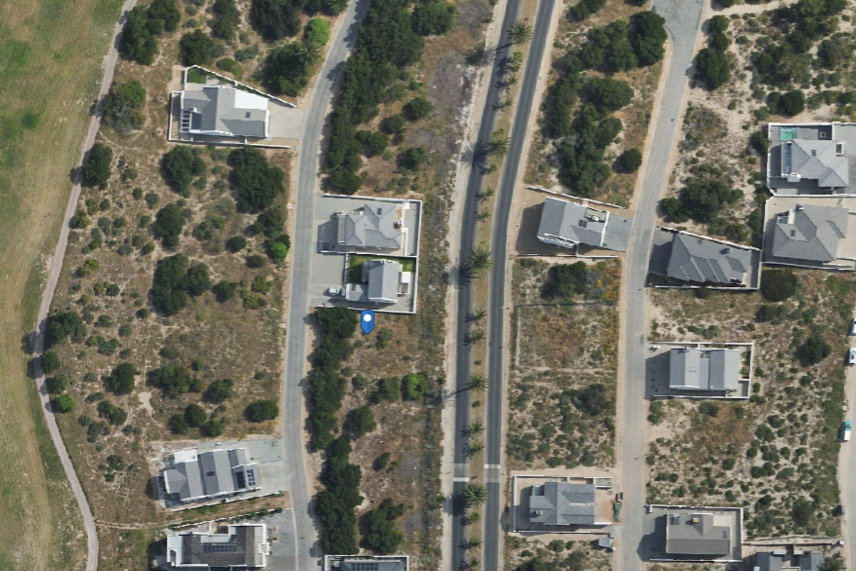 An aerial view of a vacant residential plot situated within a developed coastal estate, featuring established road access and surrounding residential properties.