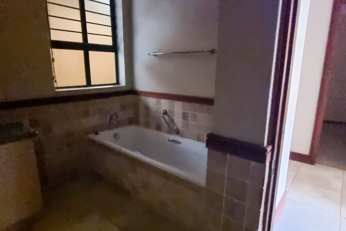 A functional bathroom featuring a built-in bathtub with tiled surround, vanity cabinet, and a window with security bars.