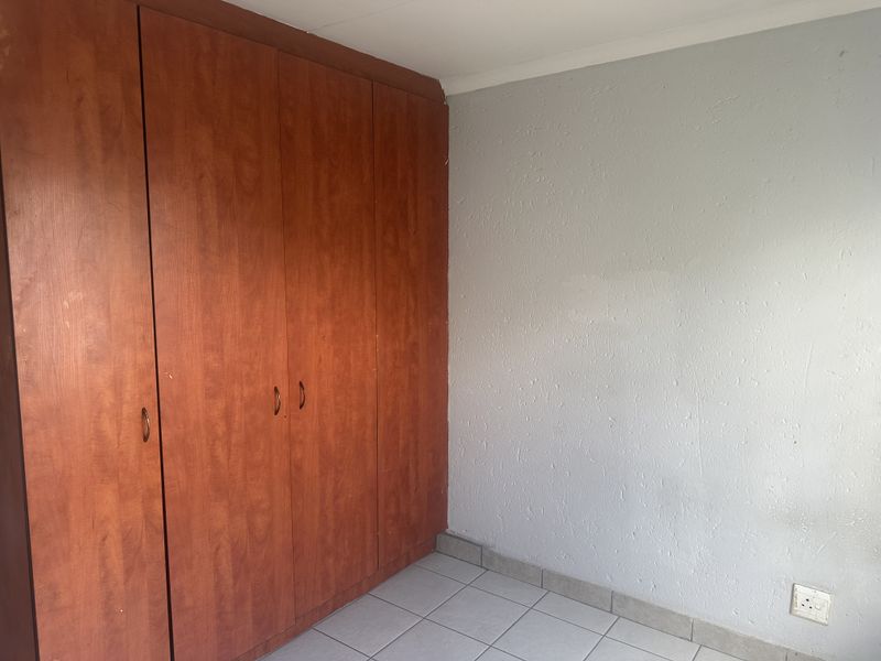 A vacant bedroom featuring built-in wooden cupboards and tiled flooring, offering a blank canvas for potential updates and interior design.