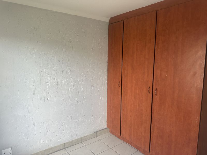 A bedroom featuring tiled flooring and built-in wooden cupboards with a textured wall finish.