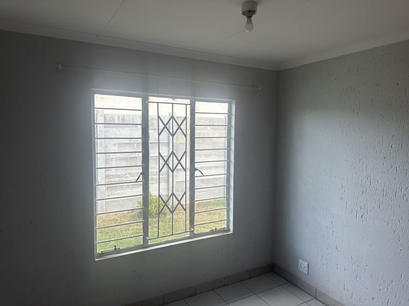 An empty bedroom featuring tiled flooring, security bars on the window, and neutral wall finishes, providing a blank canvas for potential interior design.