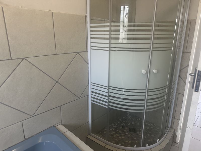A bathroom featuring a corner shower cubicle and a bathtub with dated wall tiling and fixtures, offering potential for a modern renovation.