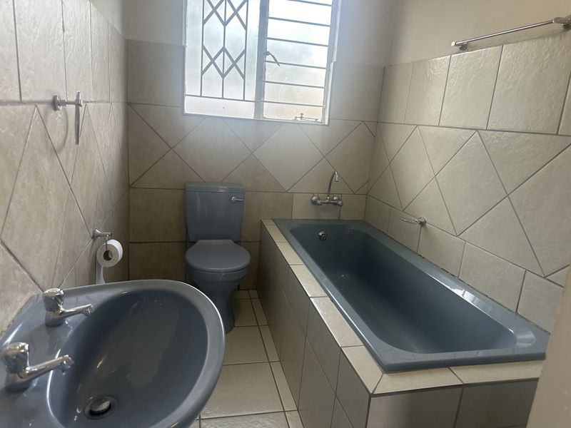 A functional bathroom featuring a built-in bathtub, toilet, and pedestal basin with neutral wall and floor tiling.