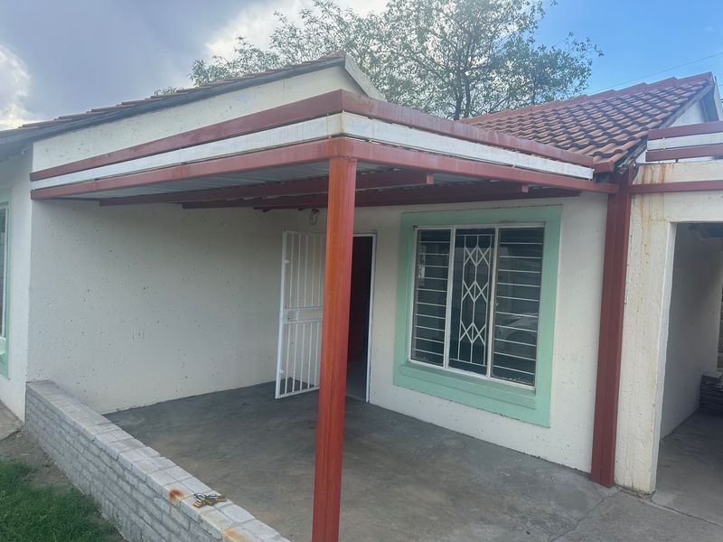 A covered patio area featuring a metal roof structure, security gate, and security bars on the windows, showing signs of weathering and rust.