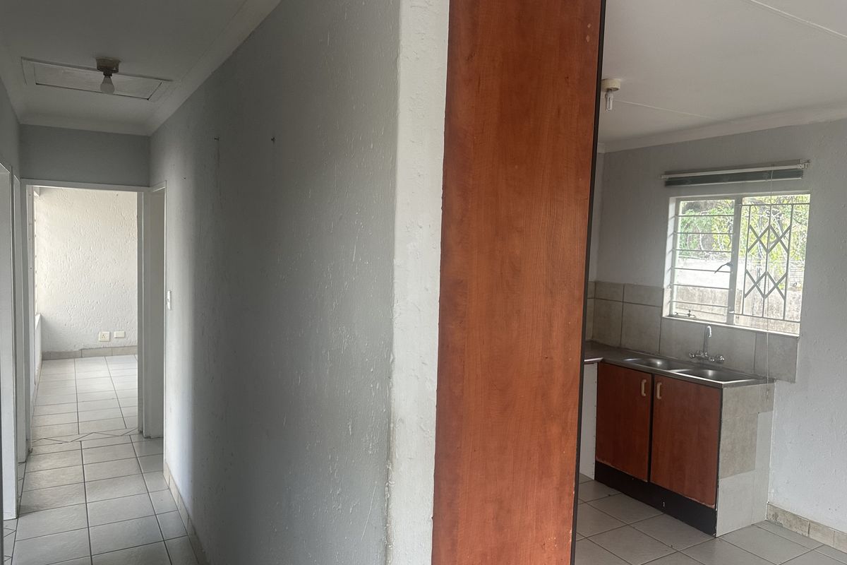 A functional kitchen area featuring built-in cabinetry, a double sink, and tiled flooring, leading into a hallway with access to additional living space.