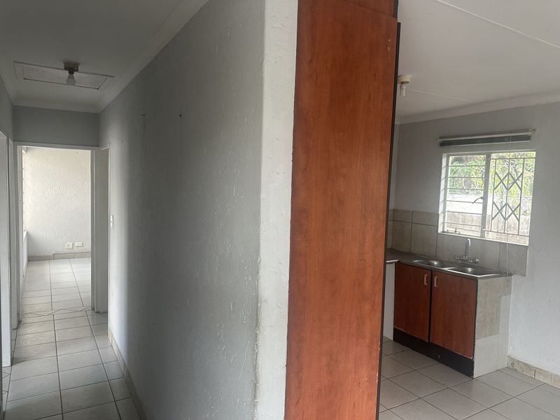 A functional kitchen area featuring built-in cabinetry, a double sink, and tiled flooring, leading into a hallway with access to additional living space.