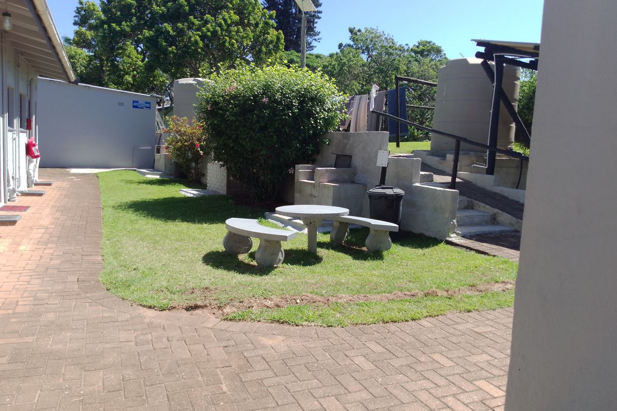 A communal outdoor area featuring paved walkways, a small lawn, built-in concrete seating, and water storage tanks.