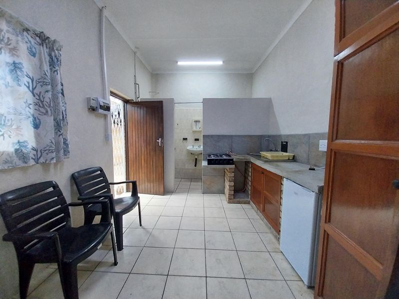 A functional kitchen area featuring tiled floors, a built-in brick counter with a gas hob, and a small sink, with an adjacent bathroom access.
