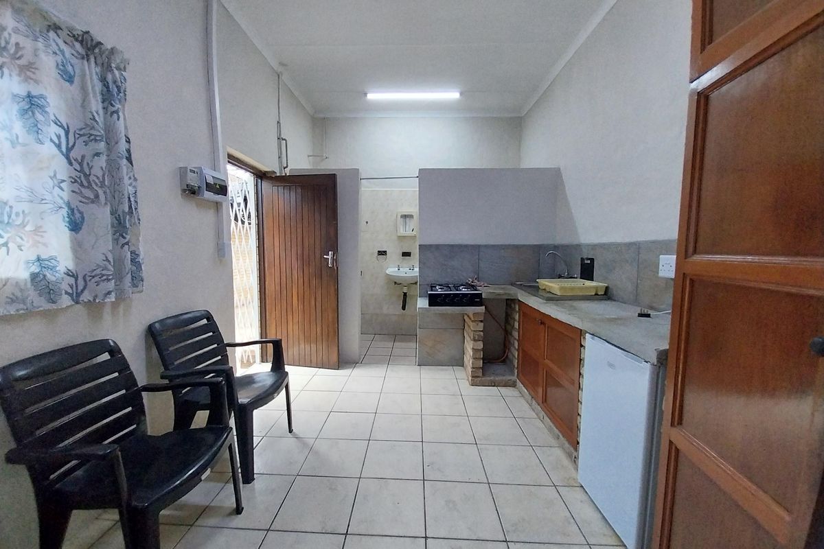 A functional kitchen area featuring tiled floors, a built-in brick counter with a gas hob, and a small sink, with an adjacent bathroom access.