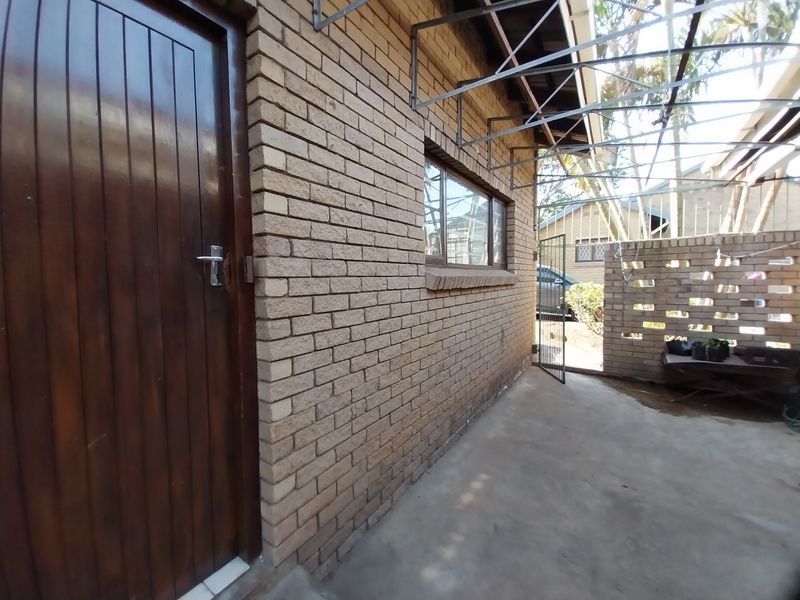 A side view of the cottage featuring a brick facade, timber entrance door, and a covered concrete patio area with a decorative brick screen wall.