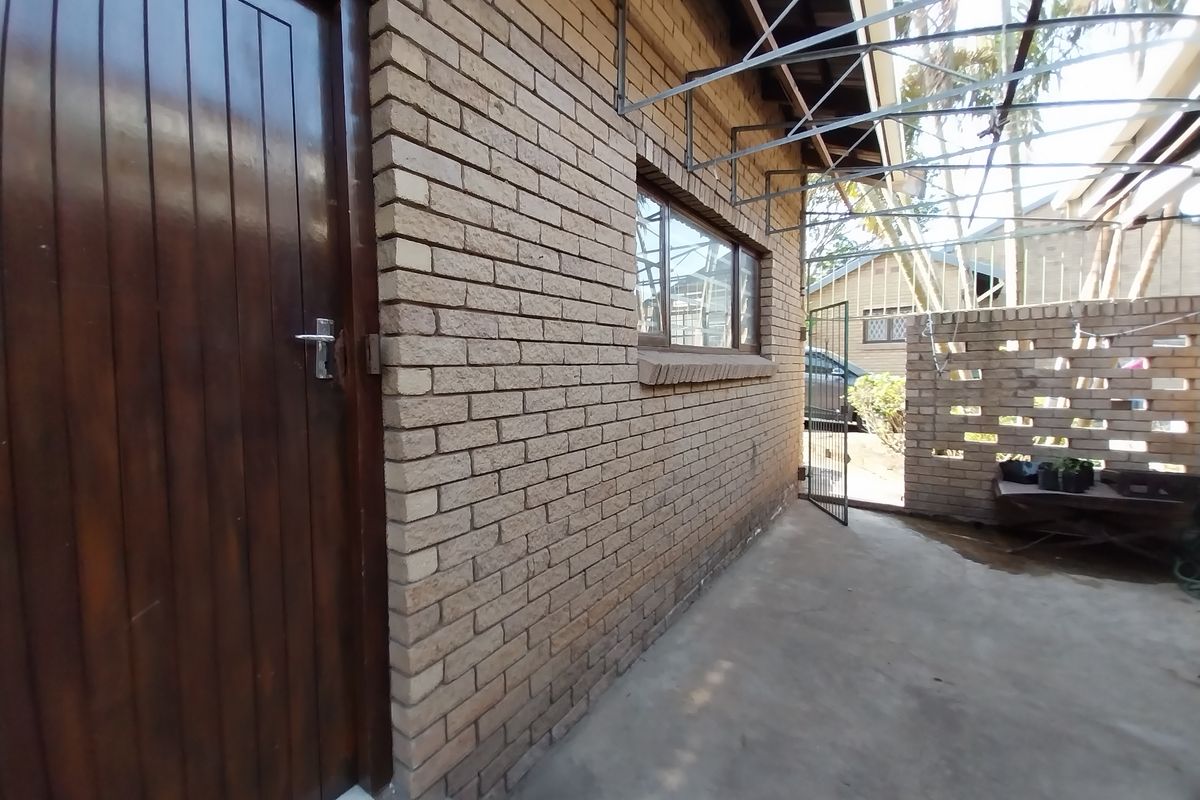 A side view of the cottage featuring a brick facade, timber entrance door, and a covered concrete patio area with a decorative brick screen wall.