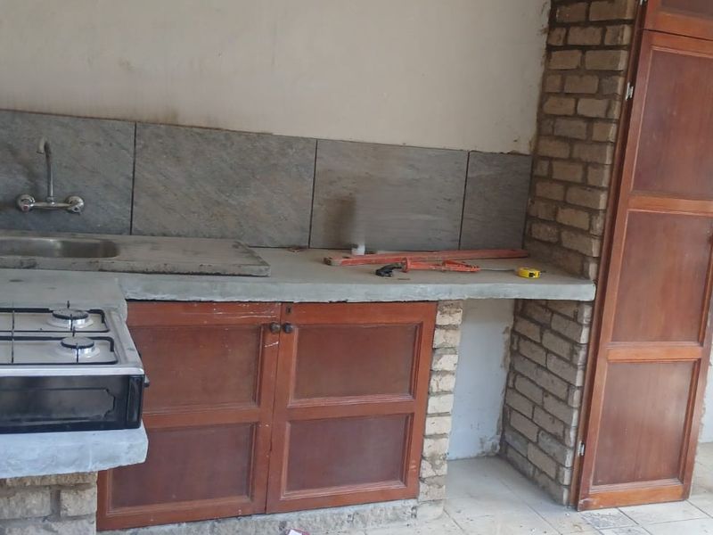 A rustic kitchen area featuring built-in cabinetry, a concrete countertop, a stainless steel sink, and a gas hob, requiring cosmetic updates and finishing touches.