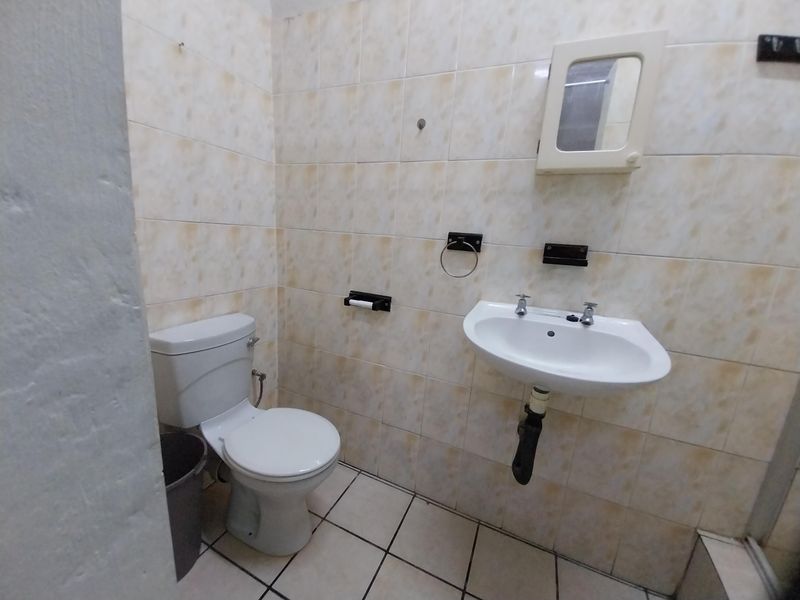 A functional bathroom featuring a pedestal washbasin, toilet, and wall-mounted medicine cabinet, finished with dated ceramic wall and floor tiles.