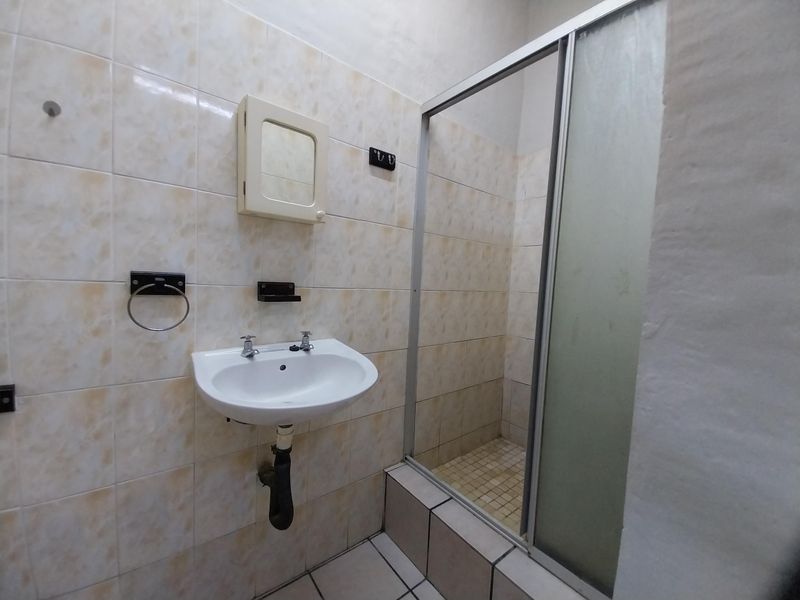 A functional bathroom featuring a wall-mounted basin, shower enclosure, and tiled finishes, offering potential for modernization and aesthetic updates.