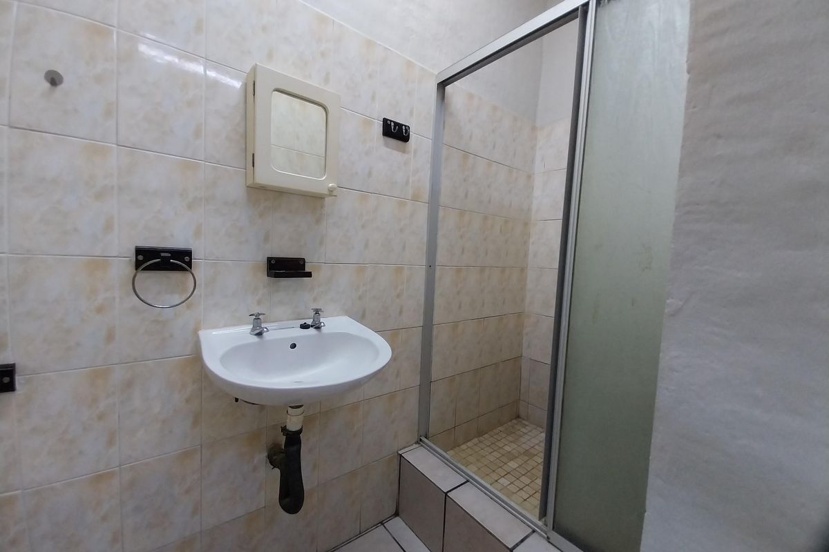 A functional bathroom featuring a wall-mounted basin, shower enclosure, and tiled finishes, offering potential for modernization and aesthetic updates.