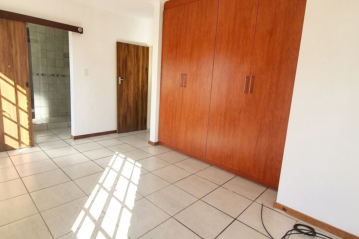 A bright, empty bedroom featuring tiled flooring, built-in wooden cupboards, and a sliding door leading to an en-suite bathroom area.