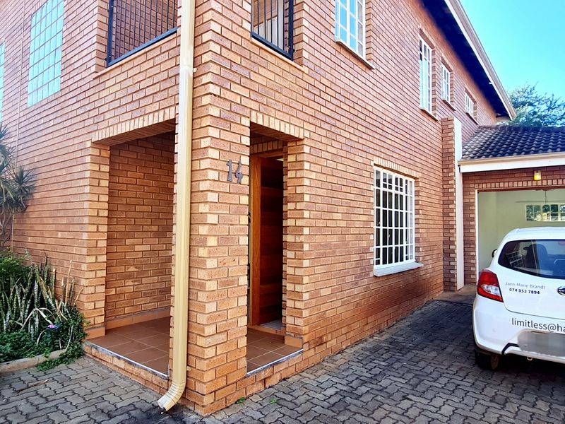 Front exterior view of a facebrick townhouse featuring a paved driveway, covered entrance, and an integrated garage.