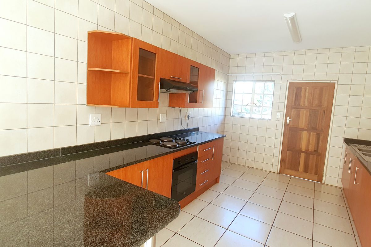 A functional kitchen featuring wooden cabinetry, granite countertops, a built-in oven, hob, and extractor fan, with tiled walls and flooring throughout.